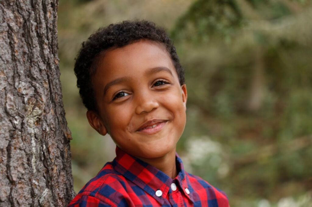 Warm outdoor portrait of a smiling child beside a tree